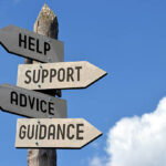 Wooden singpost with "help, support, advice, guidance" arrows against blue sky.